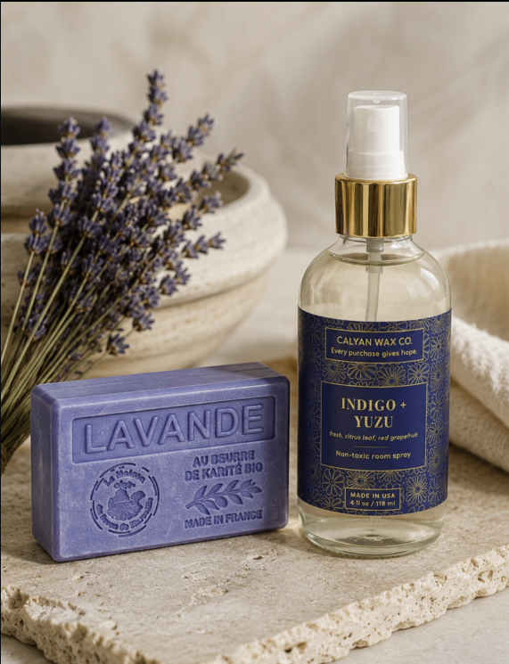 A bottle of Calyan Wax Co Indigo + Yuzu room spray and a lavender hand soap bar are styled on a stone surface with dried lavender and a neutral background.